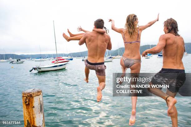 group of young adults jump off a wharf into the water. - pittwater stock pictures, royalty-free photos & images