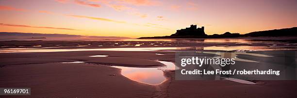 bamburgh castle in silhouette at sunrise, with rock pools on empty beach, northumberland, england, united kingdom, europe - northumberland stock pictures, royalty-free photos & images
