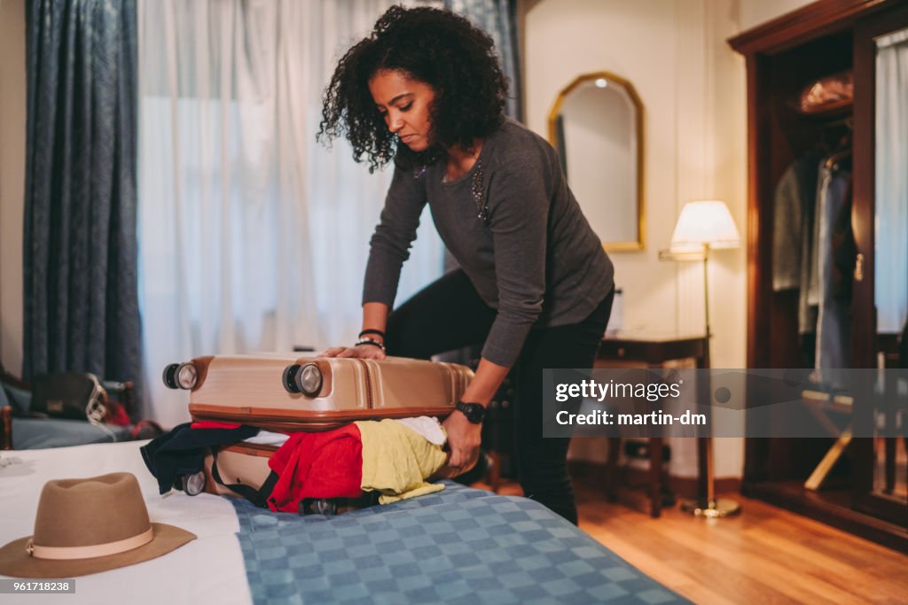 Mujer de raza mixta con desbordante maleta antes de viaje