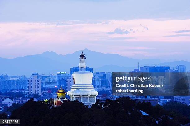 an illuminated white pagoda and city buildings at sunset, beihai park, beijing china - beihai park stockfoto's en -beelden