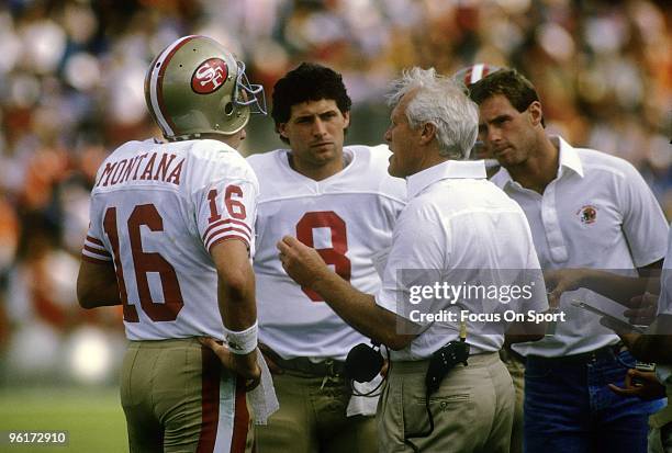 Quarterbacks Joe Montana, and Steve Young of the San Francisco 49ers on the sideline talking with head coach Bill Walsh during an NFL football game...