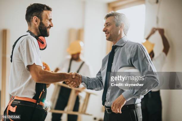 happy manual workers shaking hands with an architect at construction site. - inspectors stock pictures, royalty-free photos & images