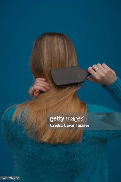 rear view of woman brushing hair against blue background - woman brushing hair stockfoto's en -beelden