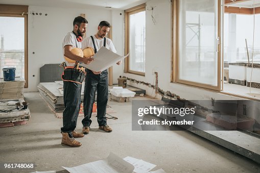 Lunghezza completa dei lavoratori edili che analizzano i progetti nell'appartamento. Lunghezza completa dei lavoratori edili che analizzano i progetti nell'appartamento.