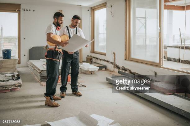 lunghezza completa dei lavoratori edili che analizzano i progetti nell'appartamento. - appartamento foto e immagini stock