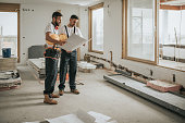 Full length of construction workers analyzing blueprints in the apartment.