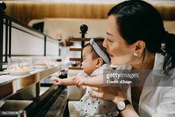 young asian mother and cute baby dining in japanese restaurant joyfully - sushi restaurant stockfoto's en -beelden