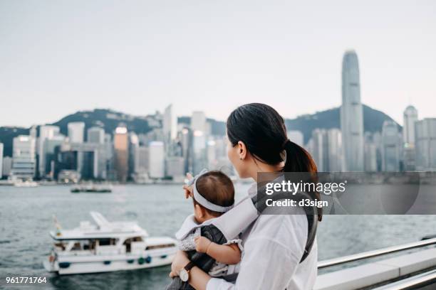 mother and baby girl enjoying the beautiful city skyline of hong kong by the promenade - hong kong family stockfoto's en -beelden