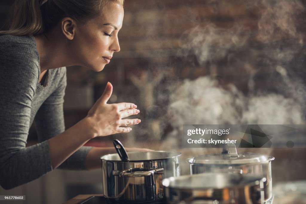 Beautiful woman smelling delicious lunch she is preparing in the kitchen.