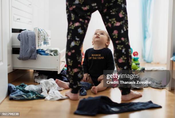 1 year old boy throws out clothes from wooden furniture at home - thanasis zovoilis stock pictures, royalty-free photos & images