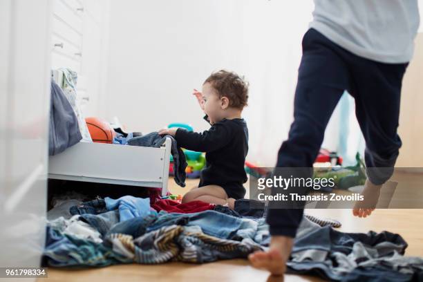 1 year old boy throws out clothes from wooden furniture at home - thanasis zovoilis stock pictures, royalty-free photos & images