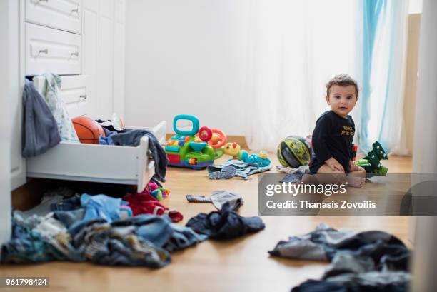 1 year old boy throws out clothes from wooden furniture at home - thanasis zovoilis stock pictures, royalty-free photos & images