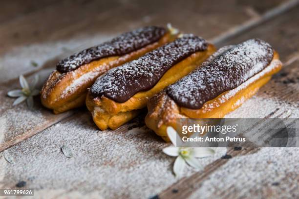 traditional french dessert. eclair with chocolate icing in powdered sugar - relámpago de crema fotografías e imágenes de stock