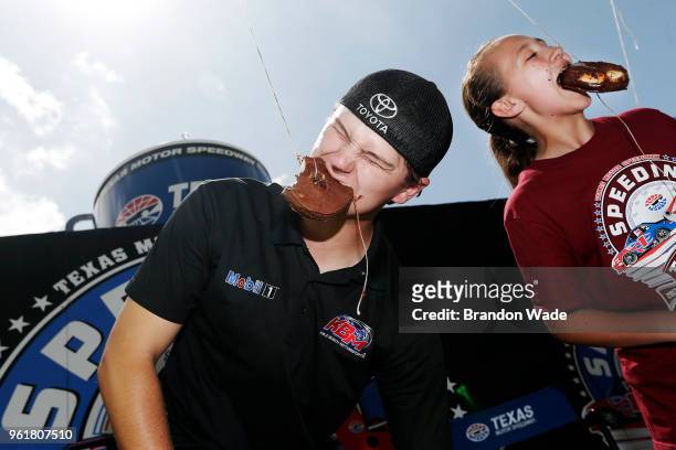 Driver Todd Gilliland, left, competes in a donut on a string eating contest against elementary school students during the Speeding To Read at Texas...