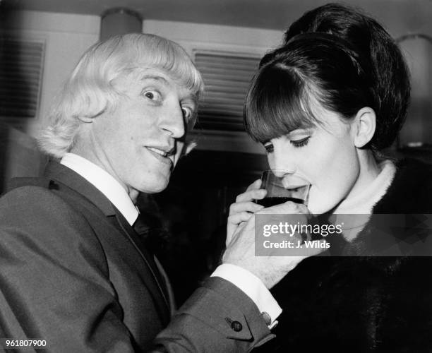 English singer Sandie Shaw accepts a drink from disc jockey Jimmy Savile at a Variety Club of Great Britain luncheon at the Savoy Hotel in London,...