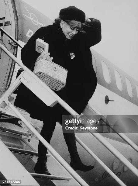 American actress Gloria Swanson arrives at Zurich Airport in Switzerland by air, carrying a book on dianetics, 10th January 1968.