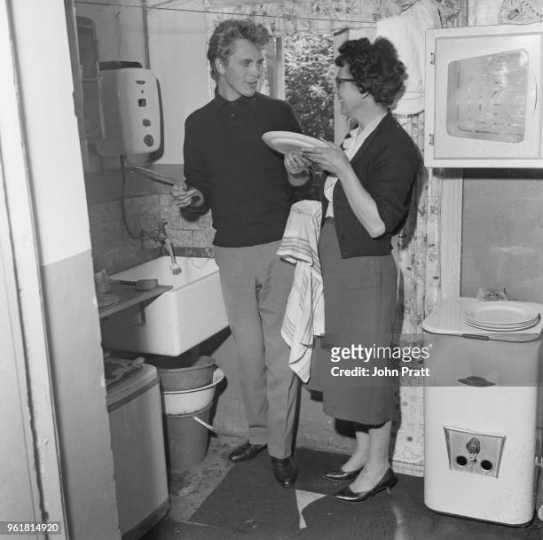 English actor Terence Stamp helps his mother Ethel with the dishes at their house in Plaistow, London, 28th May 1961. He has been chosen by Peter...