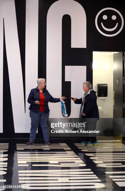 Museum visitor hands her smart phone to her friend as they stand in an art installation by Barbara Kruger which includes words and phrases printed on...