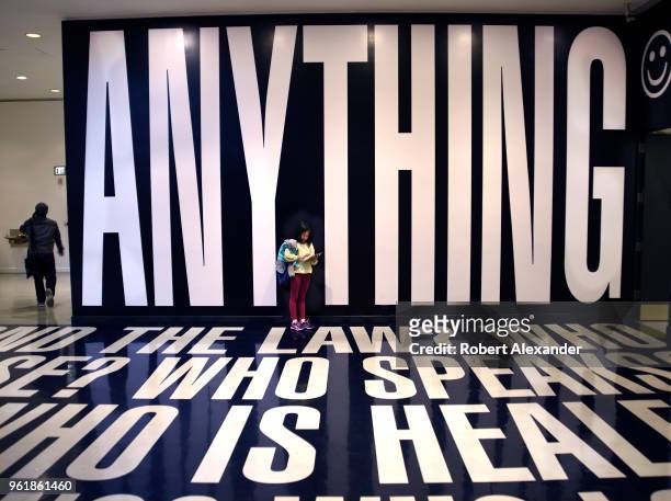 Young girl uses her mobile device as she stands in an art installation by Barbara Kruger which includes words and phrases printed on the floor and...