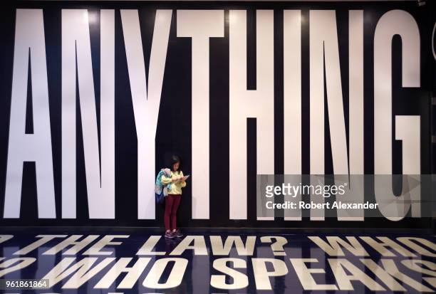 Young girl uses her mobile device as she stands in an art installation by Barbara Kruger which includes words and phrases printed on the floor and...