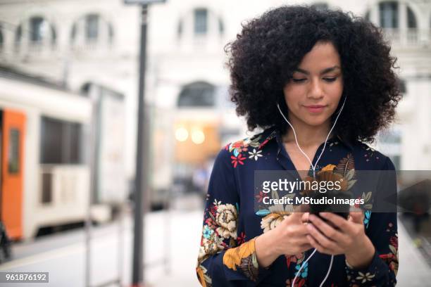 woman at the train station using mobile phone. - listening imagens e fotografias de stock