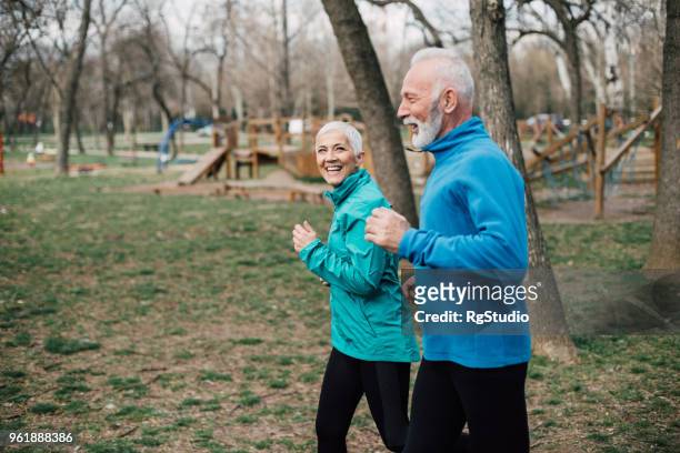 senior couple wearing sport clothes jogging at the park - blue jacket stock pictures, royalty-free photos & images