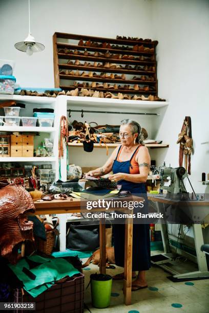 leather shop owner looking at pieces of leather while designing handbag in workshop - large group of craftsman stock-fotos und bilder