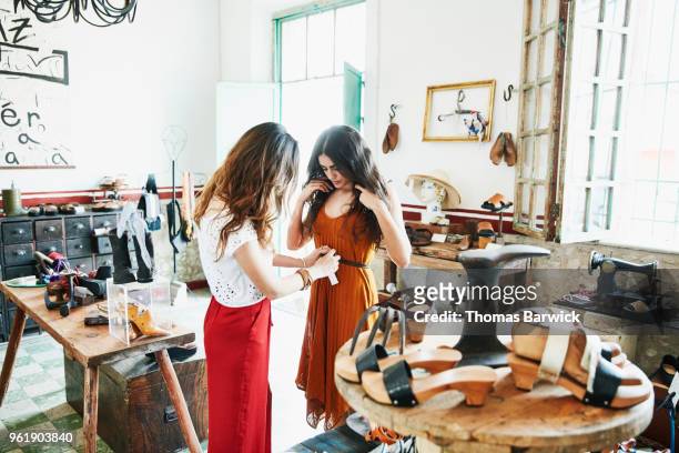 woman helping friend try on handmade leather belt while shopping together in boutique - cinturón rojo fotografías e imágenes de stock