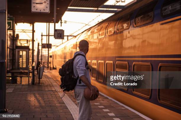 jonge mannelijke student van de niet-blanke uitvoering van een basketbal terwijl te wachten op een europese treinstation op een mooie avond - non urban scene stockfoto's en -beelden