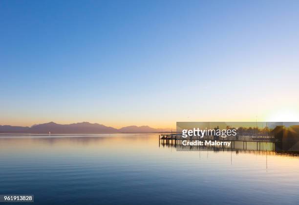 view over lake chiemsee with landing stage at sunset with mountain range in the background. chiemgau, bavaria, germany - lake chiemsee 個照片及圖片檔