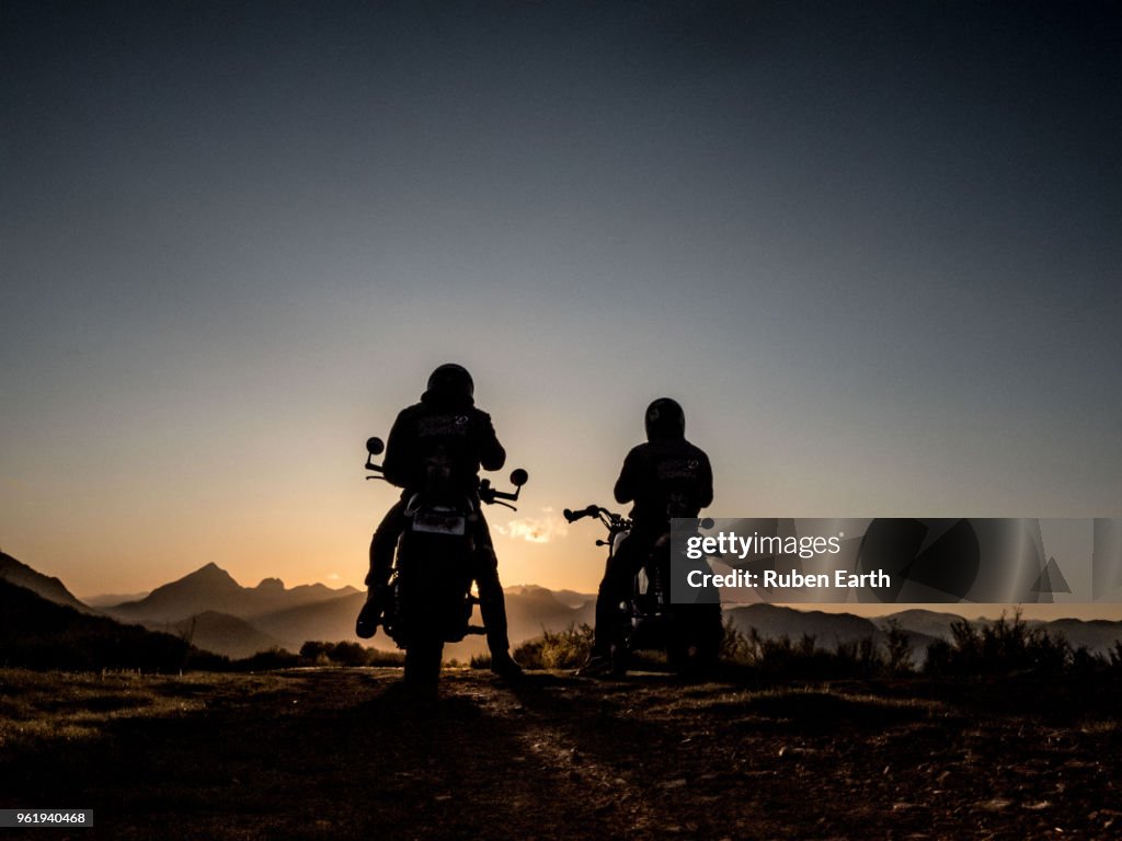 Two motorcycles and riders looking at the mountains