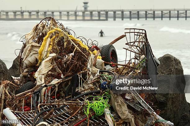 Surfer passes trash and debris from the run-off of recent storms near the mouth of the San Gabriel River as another storm moves in on January 26,...