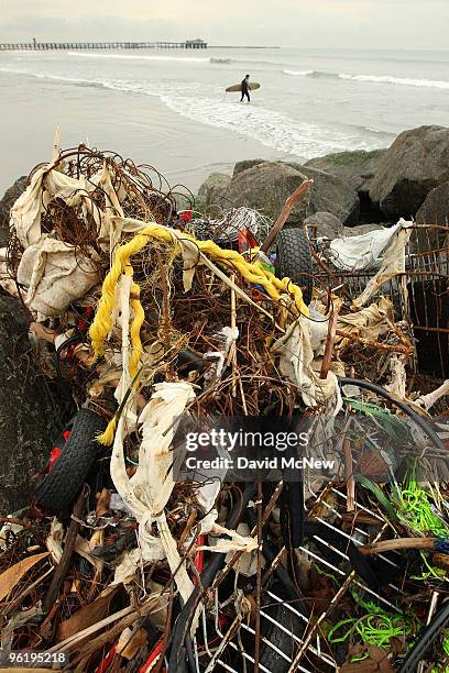 Surfer passes trash and debris from the run-off of recent storms near the mouth of the San Gabriel River as another storm moves in on January 26,...