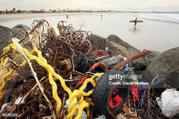 Surfer passes trash and debris from the run-off of recent storms near the mouth of the San Gabriel River as another storm moves in on January 26,...