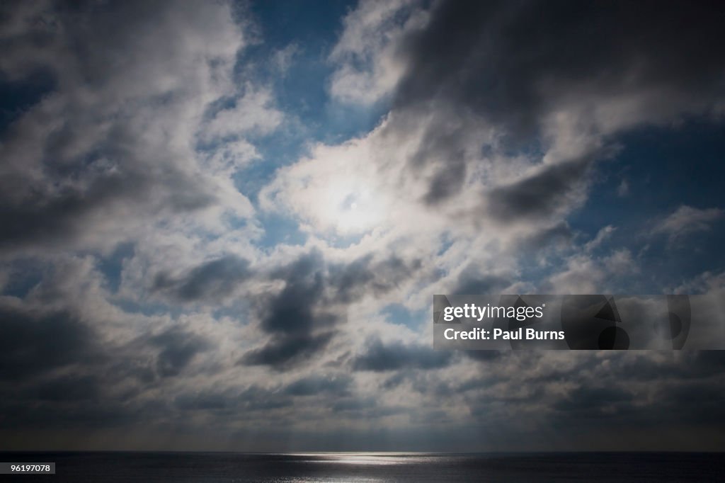 Sun behind clouds above the ocean