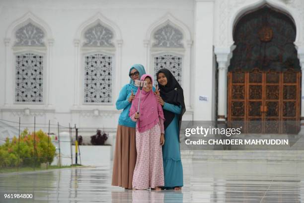 Indonesian Muslim women take selfies after praying at the Baiturrahman mosque in Banda Aceh on May 24, 2018. Muslims throughout the world are marking...