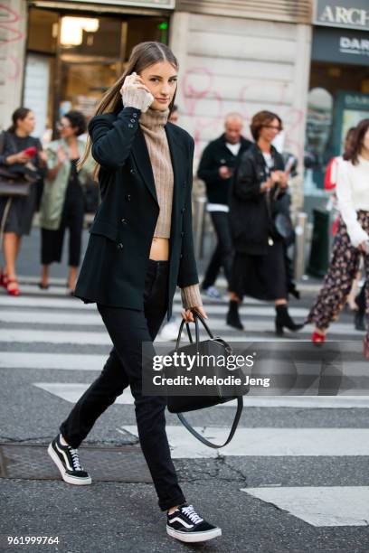 Model Rachel Fox talks on the phone and wears a black blazer, pants, Vans sneakers, and Givenchy bag with a light brown cropped sweater top during...