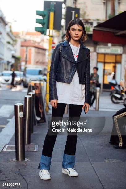 Model Milena Litvinovskaya wears a cropped black leather jacket, white top, blue pants with jean ankles, and white Tory Burch sneakers during Milan...