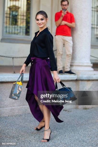 Model Grace Elizabeth twirls and wears a black blouse, purple asymmetrical skirt, black bag, and black heels after the Alberta Ferretti show during...