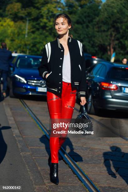 Model Grace Elizabeth wears a blue varsity jacket, white tshirt, and red motorcycle leather ribbed and zip leggings, a black bag, and black pants...