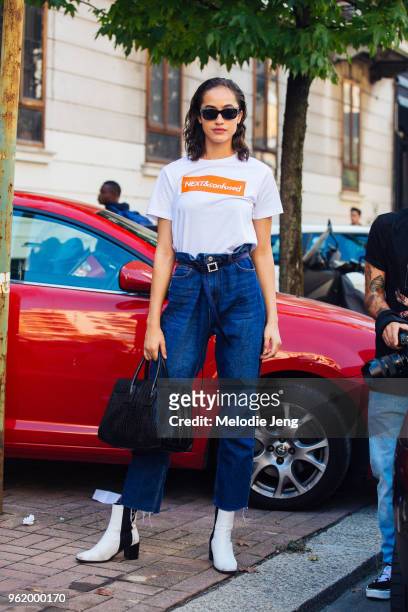 Model Alanna Arrington wears black sunglasses, a Next Models "NEXT&confused" tshirt, blue jeans, an Hermes bag ,and black and white booties during...