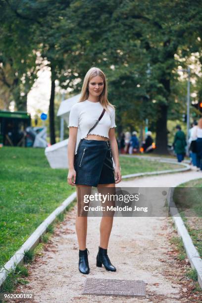 Model Anna Ewers wears a cropped fitted white top, black leather mini skirt, and black boots during Milan Fashion Week Spring/Summer 2018 on...