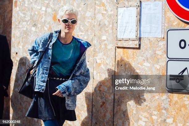 Model Taja Feistner wears white alien-style sunglasses, an acid-wash denim jacket, teal top, and black skirt during Milan Fashion Week Spring/Summer...