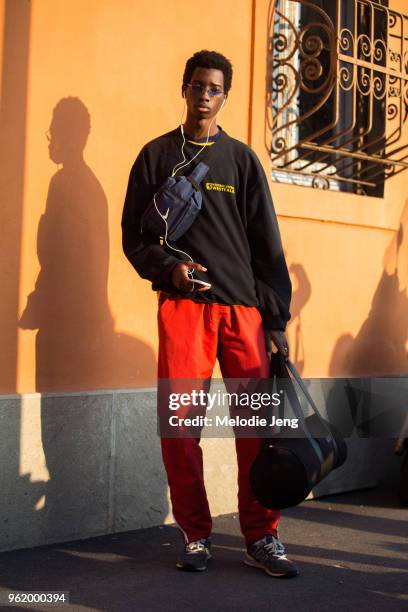 Model Benoit Michel listens to music with earphones and wears blue sunglasses, a blue Nike fannypack, black sweatshirt, blue pants, gray New Balance...