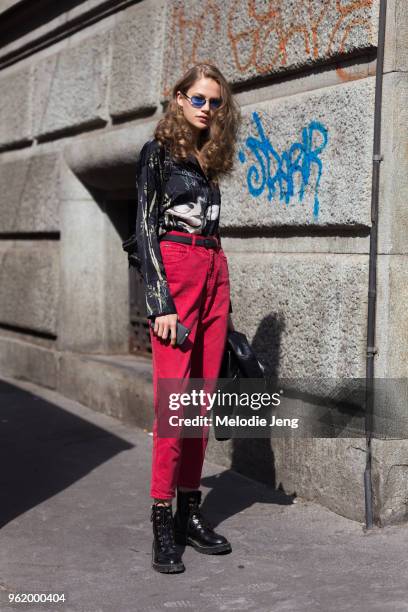 Model Ana Baryshnikova wears blue circular sunglasses, a painterly black shirt with ducks, red pants, and black boots during Milan Fashion Week...