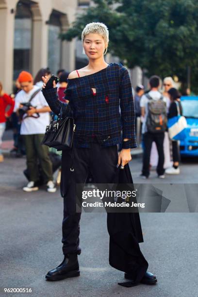 Model Manami Kinoshita wears a distressed blue plaid top, black purse, black pants, black boots, and carries a MSGM shirt during Milan Fashion Week...