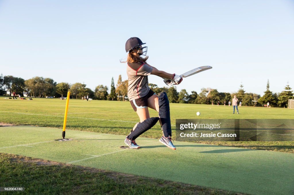A female crickets bats on a sports field in the evening light