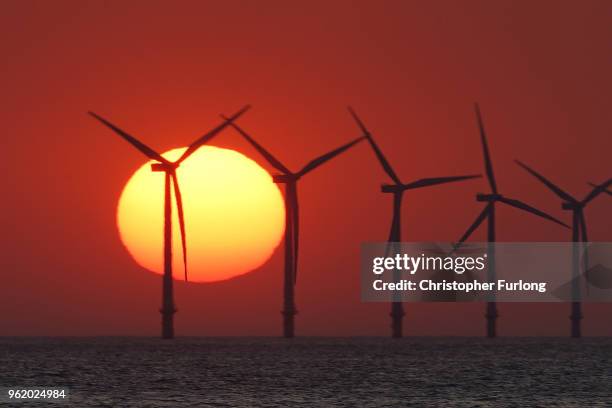 The sun sets behind the wind turbines of Burbo Bank Offshore Wind Farm in the Irish Sea on May 23, 2018 in Wallasey, England.