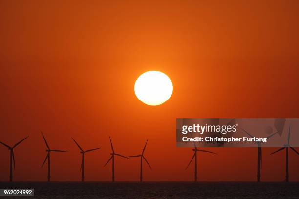 The sun sets behind the wind turbines of Burbo Bank Offshore Wind Farm in the Irish Sea on May 23, 2018 in Wallasey, England.