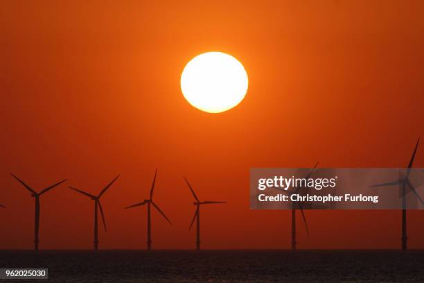 The sun sets behind the wind turbines of Burbo Bank Offshore Wind Farm in the Irish Sea on May 23, 2018 in Wallasey, England.